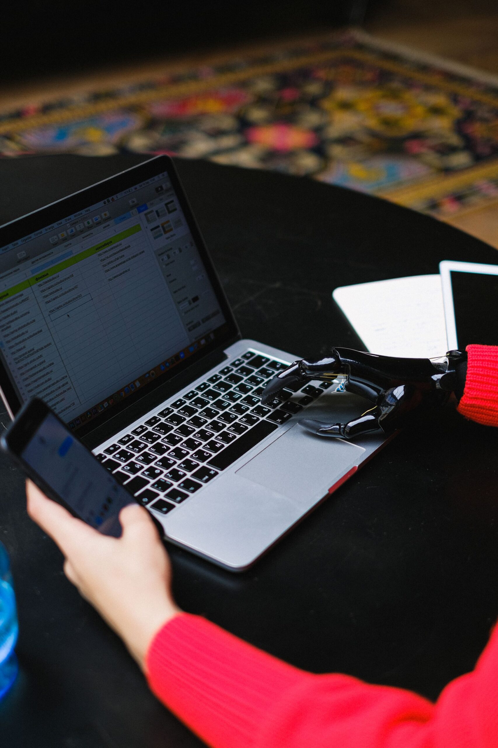 Close-up of a person with a prosthetic hand typing on a laptop while holding a phone,