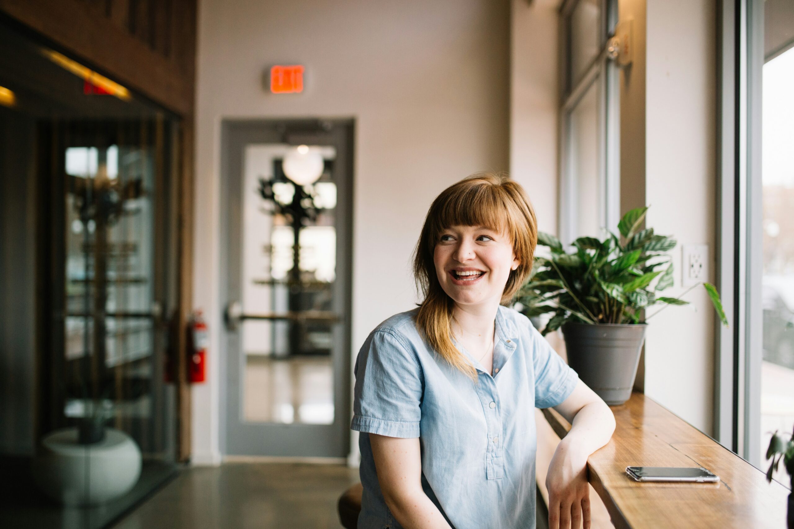 Smiling woman standing by a window with her smart phone in front of her