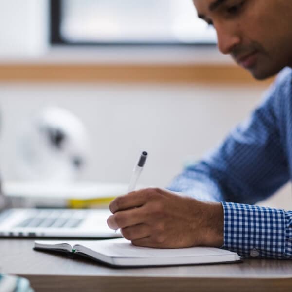 Man taking handwritten notes in front of a computer
